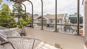 Un balcón con una silla blanca, una planta en maceta y vistas de edificios residenciales.