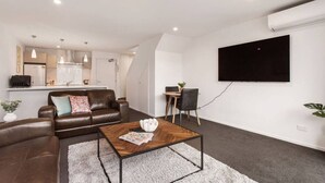 Un salon moderne avec un canapé en cuir marron, une table basse en bois et un téléviseur à écran plat fixé au mur.