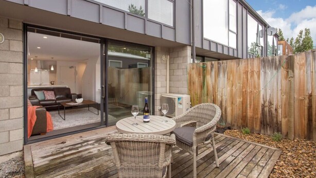 Une terrasse extérieure moderne, avec une table et des chaises, une bouteille de vin et un verre.