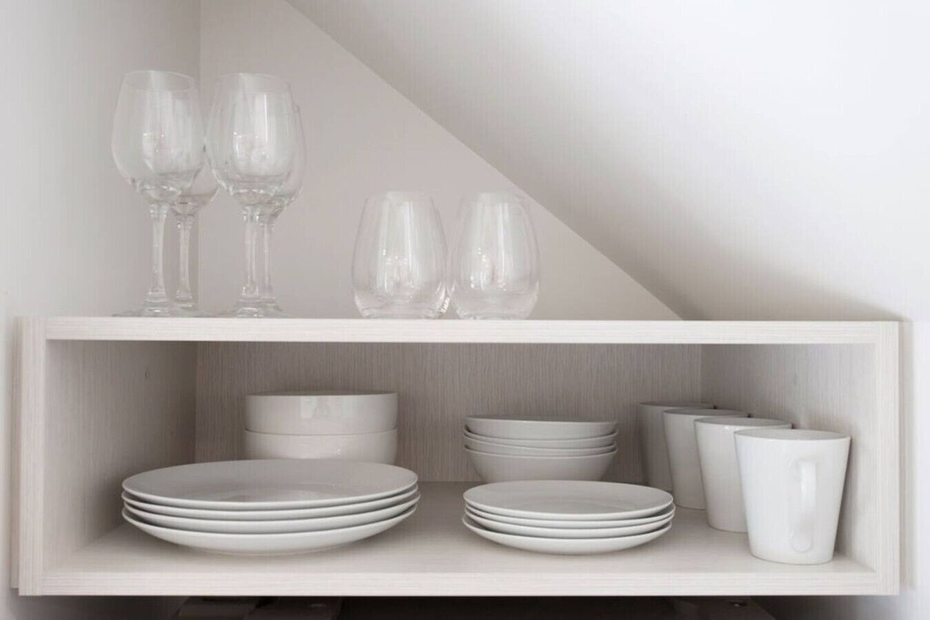 A white shelf with stacked plates and glasses.