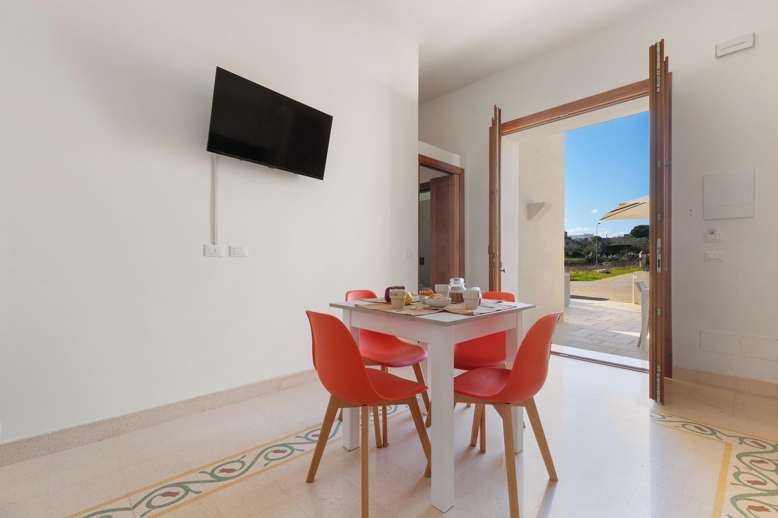 Un comedor con una mesa, sillas y un televisor de pantalla plana montado en la pared.