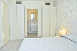 A bedroom with a bed, a nightstand, a bedside lamp, and a bathroom visible through an open door. - Relax Vibes Near the Beach (San Michele al Tagliamento)