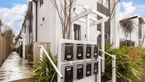 Un immeuble résidentiel à la façade blanche, doté d’une entrée abritée avec des boîtes aux lettres numérotées et d’un chemin en béton menant à l’entrée.