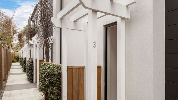 Une rangée de bâtiments modernes, blancs, avec une clôture en bois et de la verdure devant.