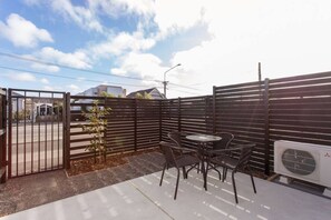 A fenced outdoor patio area with a table and chairs, an air conditioning unit, and a gate. - Brand New 2 Bedroom | Free off Street Parking (Christchurch)