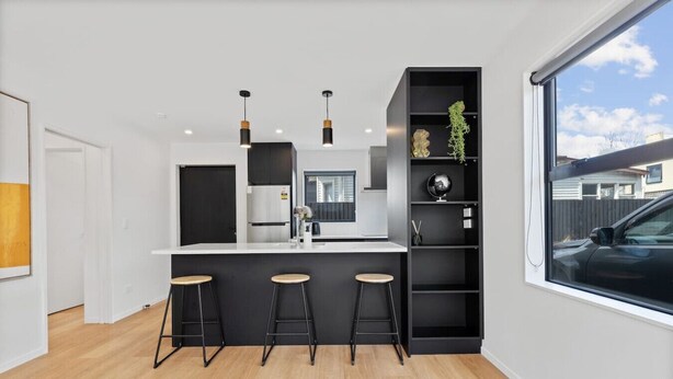 A modern kitchen with a central island, black bar stools, pendant lighting, and a view of the outside.