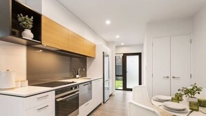 A modern kitchen with white cabinetry, stainless steel appliances, and a dining area with a white table and chairs. - Style Location New Sunny 2Bdrms Free Park (Christchurch)