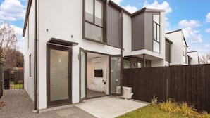 A modern two-story house with a large sliding glass door leading to a covered patio area. - Style Location New Sunny 2Bdrms Free Park (Christchurch)