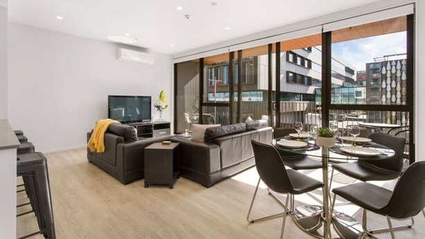 A modern living room with a sofa, TV, and dining area with chairs and a table.