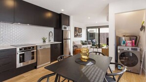 Een moderne keuken met donkere kastjes, roestvrijstalen apparatuur en een eethoek met een tafel en stoelen.