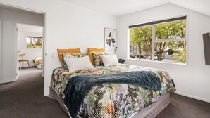 Une chambre avec un grand lit, une fenêtre donnant sur la verdure et une porte menant à une autre pièce.