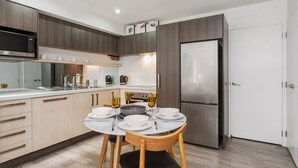 Une cuisine moderne avec un coin repas, comprenant un réfrigérateur en acier inoxydable, des armoires en bois et un plan de travail blanc.