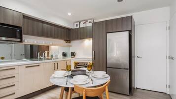 A modern kitchen with a dining area, featuring a stainless steel refrigerator, wooden cabinets, and a white countertop.