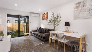 Un salon moderne comprenant un canapé, une table à manger avec des chaises, une petite table d’appoint et une plante en pot.