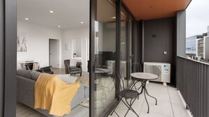 Una sala de estar moderna con un sofá, sillas y una mesa. Hay un ventanal corredero que da a un espacio exterior con una mesa y sillas.