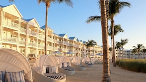 A beachfront hotel with multiple-story buildings, outdoor seating areas with umbrellas, and palm trees. - Marathon Oceanfront Suite | King Bed + Balcony (Marathon)