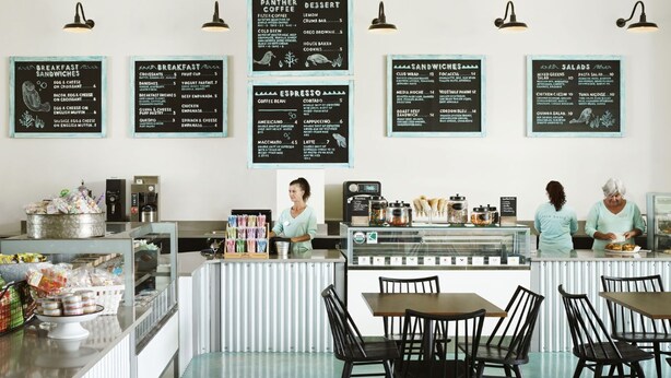 A café with multiple menu boards for breakfast, sandwiches, espresso, and desserts. There are tables and chairs for seating, and a counter with a coffee machine and food items. - Marathon Beachfront | King Bed + Veranda (Marathon)