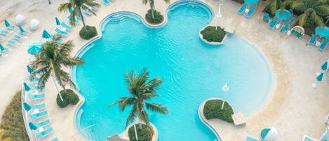 An aerial view of a resort pool with multiple sections, surrounded by palm trees and lounge chairs.