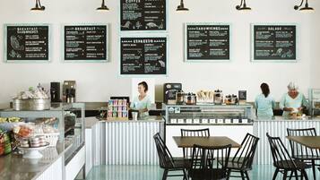 Una cafetería con varios menús que ofrecen desayuno, sándwiches, café espresso y postres. Hay mesas y sillas para sentarse, y una barra con una máquina de café y alimentos.