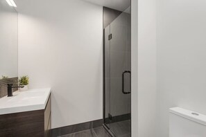A modern bathroom with a glass shower enclosure, a white sink, and a dark wood vanity.