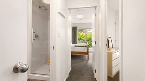 A hallway leading to a bedroom with a shower, a bed, and a bathroom with a vanity.