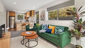 Un salon moderne avec un canapé vert, une table basse et une cuisine en arrière-plan.