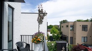 A balcony with a white brick building, a potted plant with flowers, and a black chair. - Best location in CBD, Carpark (Christchurch)