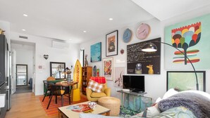 A modern living room with a sofa, a dining table, and a TV. There are clocks on the wall and a surfboard decoration. - Best location in CBD, Carpark (Christchurch)
