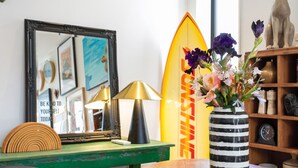 A room with a wooden table, a mirror, a surfboard, a lamp, and a vase with flowers. - Best location in CBD, Carpark (Christchurch)