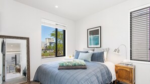 A bedroom with a large bed, a bedside table with a lamp, a framed picture on the wall, and a window with blinds. - Best location in CBD, Carpark (Christchurch)