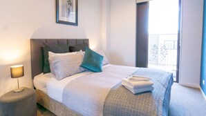 A neatly made bed with a striped bedspread and pillows, a bedside lamp, and a framed picture on the wall.