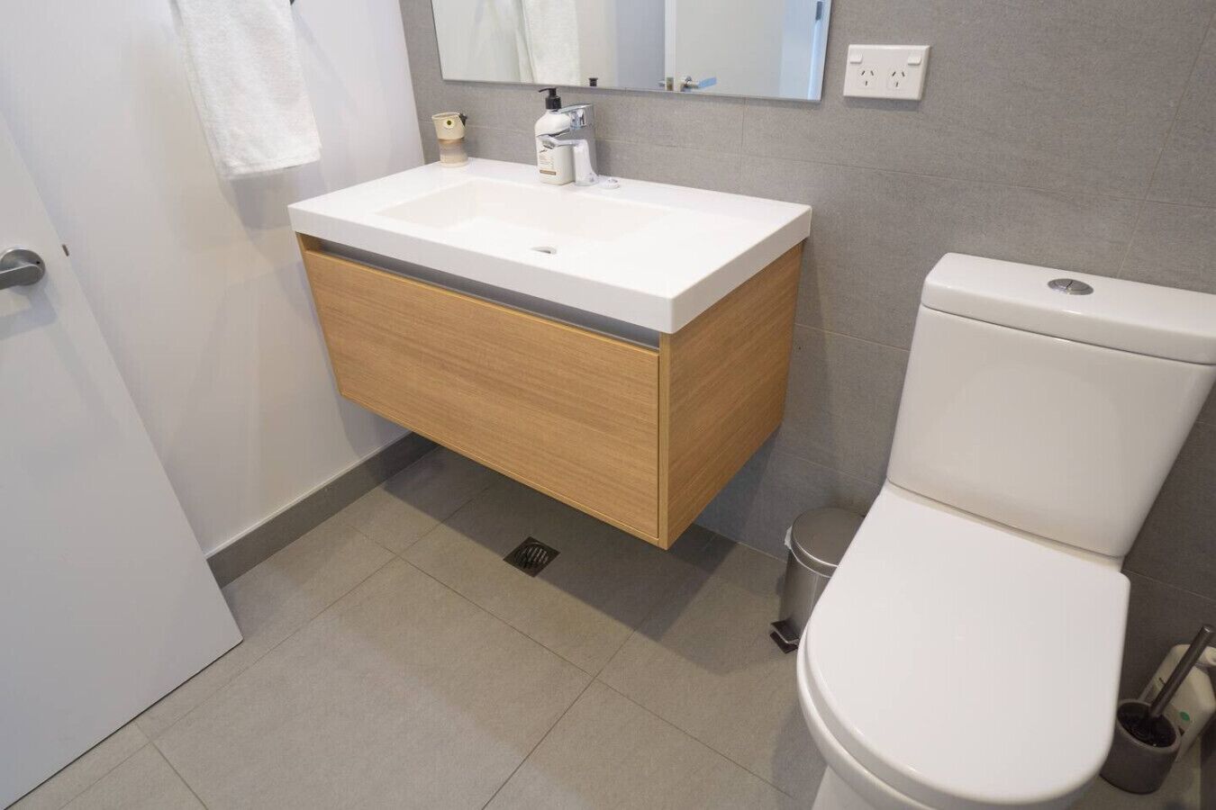 Een moderne badkamer met een witte wastafel, houten wastafelmeubel en een wit toilet.