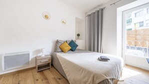 A bedroom with a bed, bedside table, and a window with curtains. - Cœur de Pau - Parking included - Le Joyau (Pau)