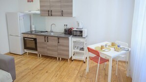 A compact kitchen with a refrigerator, oven, microwave, and a small dining area with a table and chairs. - Cœur de Pau - Parking included - Le Joyau (Pau)