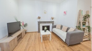 A living room with a flat-screen TV, a sofa, a coffee table, a fireplace, and a bookshelf with plants. - Cœur de Pau - Parking included - Le Joyau (Pau)