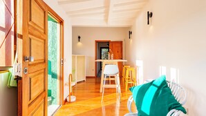 A room with a wooden door, a white chair, a wooden table, and a green pillow.