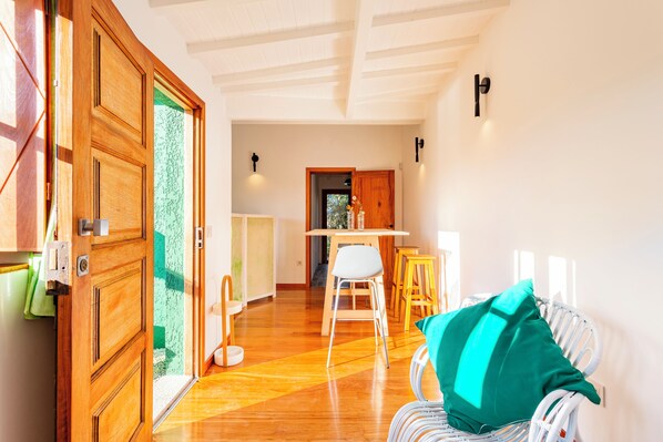 Una habitación con puerta de madera, una silla blanca, una mesa de madera y un cojín verde.