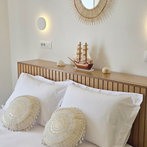 A bedroom with a wooden headboard, two decorative pillows, a ship model, and a wall-mounted mirror.
