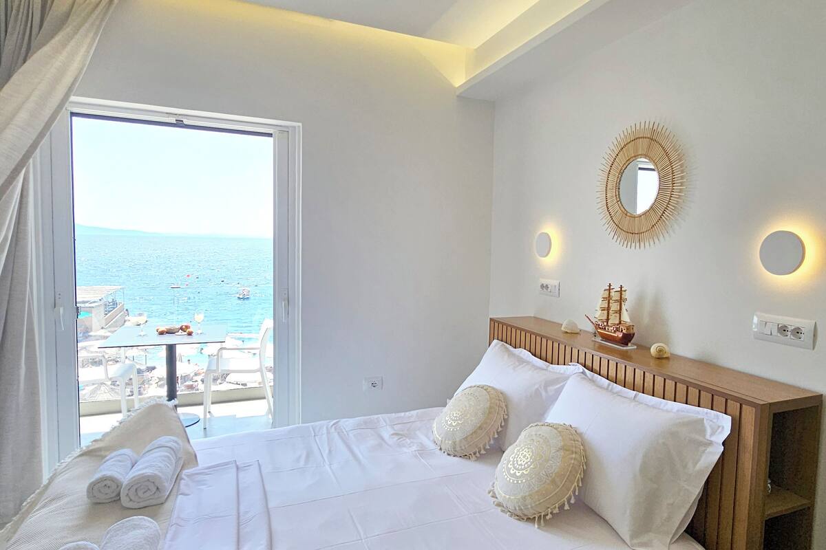 Habitación de hotel con una cama, vistas al mar, cabecero de madera y un espejo redondo en la pared.