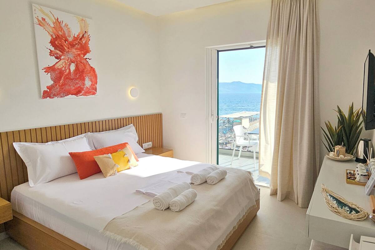 Habitación de hotel con cama, mesita de noche, escritorio con planta y vista al mar.