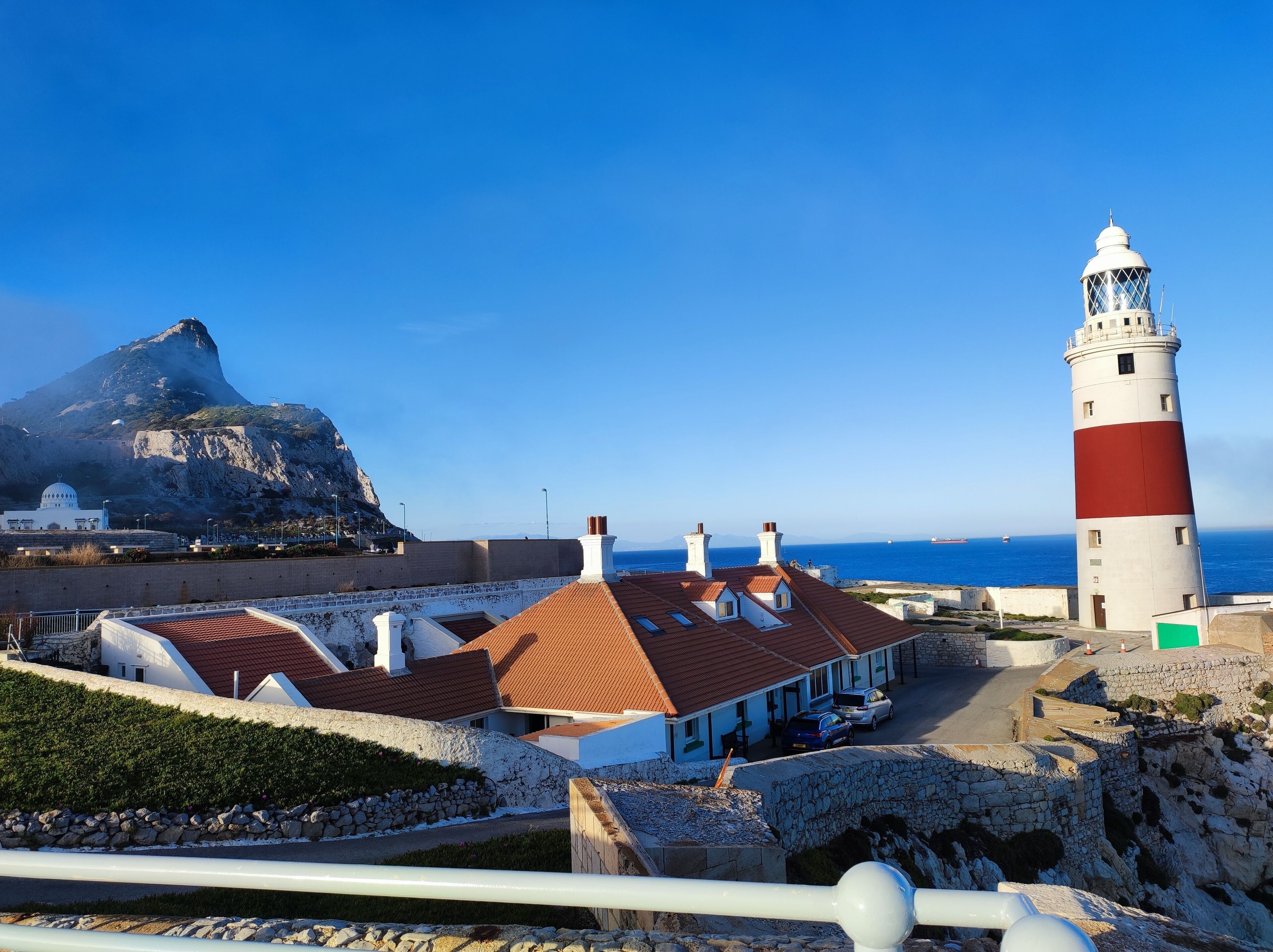 A coastal building with a red-tiled roof, a lighthouse, and a rocky cliff in the background.
