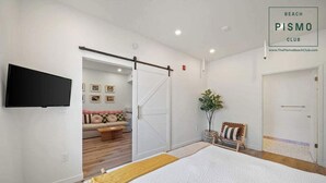 Un dormitorio con cama, una puerta corredera, televisor, planta y un banco.