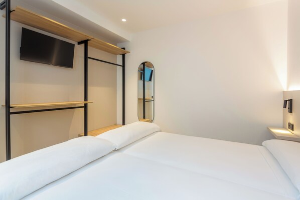 Une chambre d’hôtel avec un lit, un téléviseur fixé au mur, un miroir et une table de chevet avec une lampe.