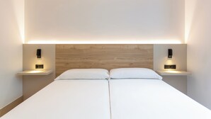 A modern hotel room with a wooden headboard, two bedside tables with integrated lighting, and a neatly made bed with white linens. - Sholeo Lodges Las Canteras Flats (Las Palmas de Gran Canaria)