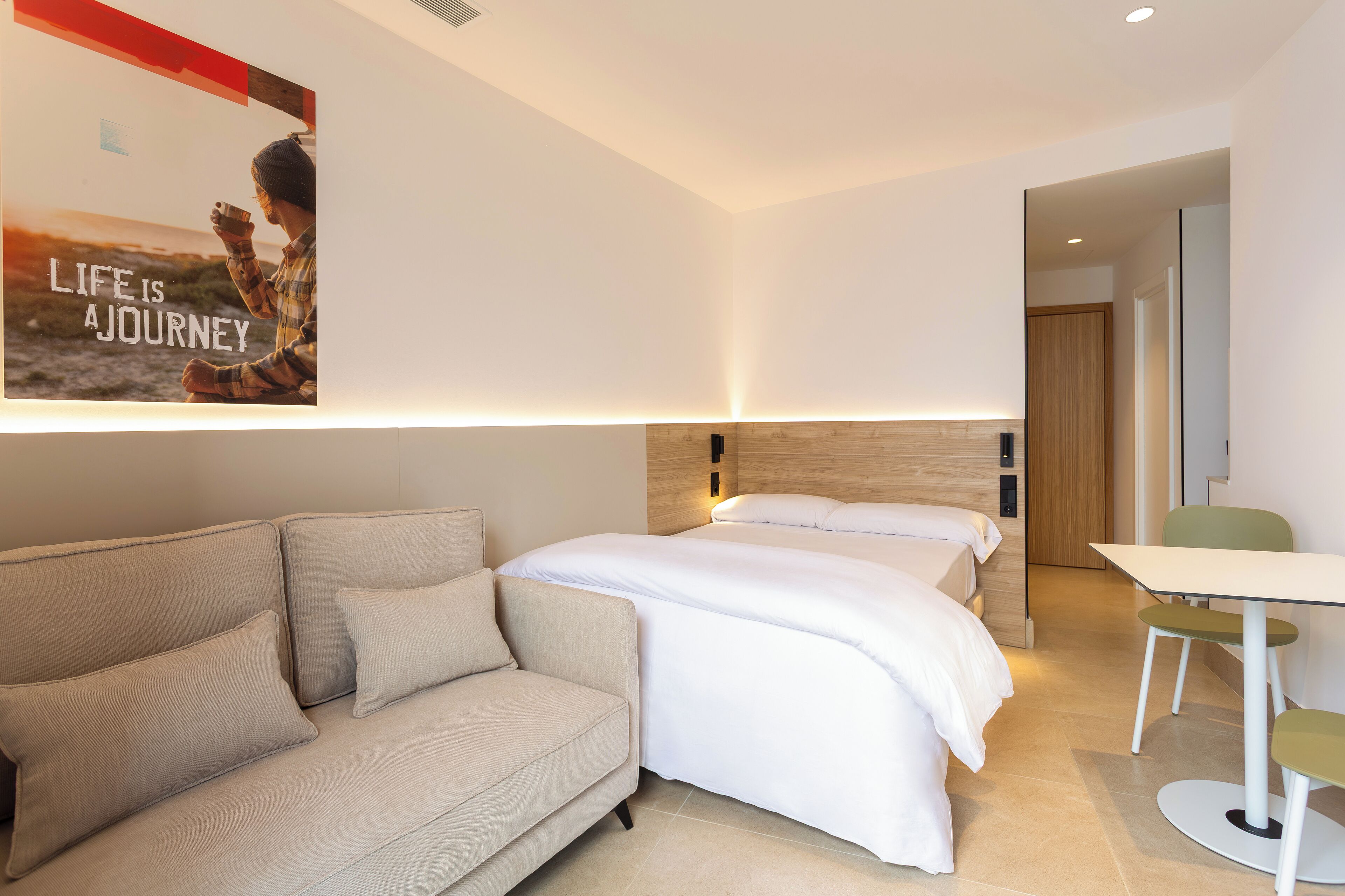 Quarto de hotel moderno com sofá, cama, uma mesinha e um pôster na parede.