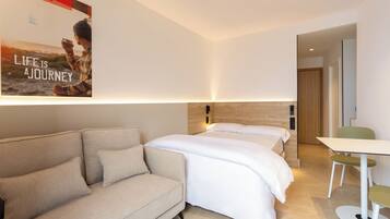 Quarto de hotel moderno com sofá, cama, uma mesinha e um pôster na parede.