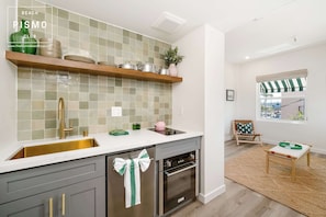A kitchen with a built-in oven, a sink, and a wooden shelf above it.