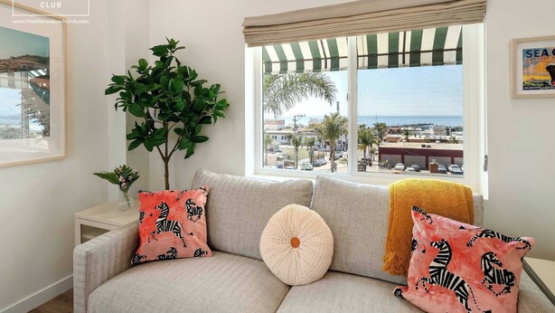 Un salon avec un canapé, une plante en pot et une fenêtre donnant sur la plage et les bâtiments.