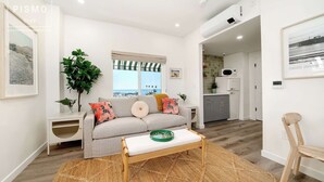 Un salon moderne avec un canapé, une table basse, une grande fenêtre donnant sur un beau paysage et une cuisine en arrière-plan.