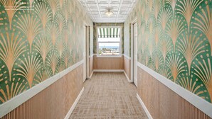 Un couloir avec un papier peint à motifs, un plancher en bois et une fenêtre donnant sur un paysage agréable.